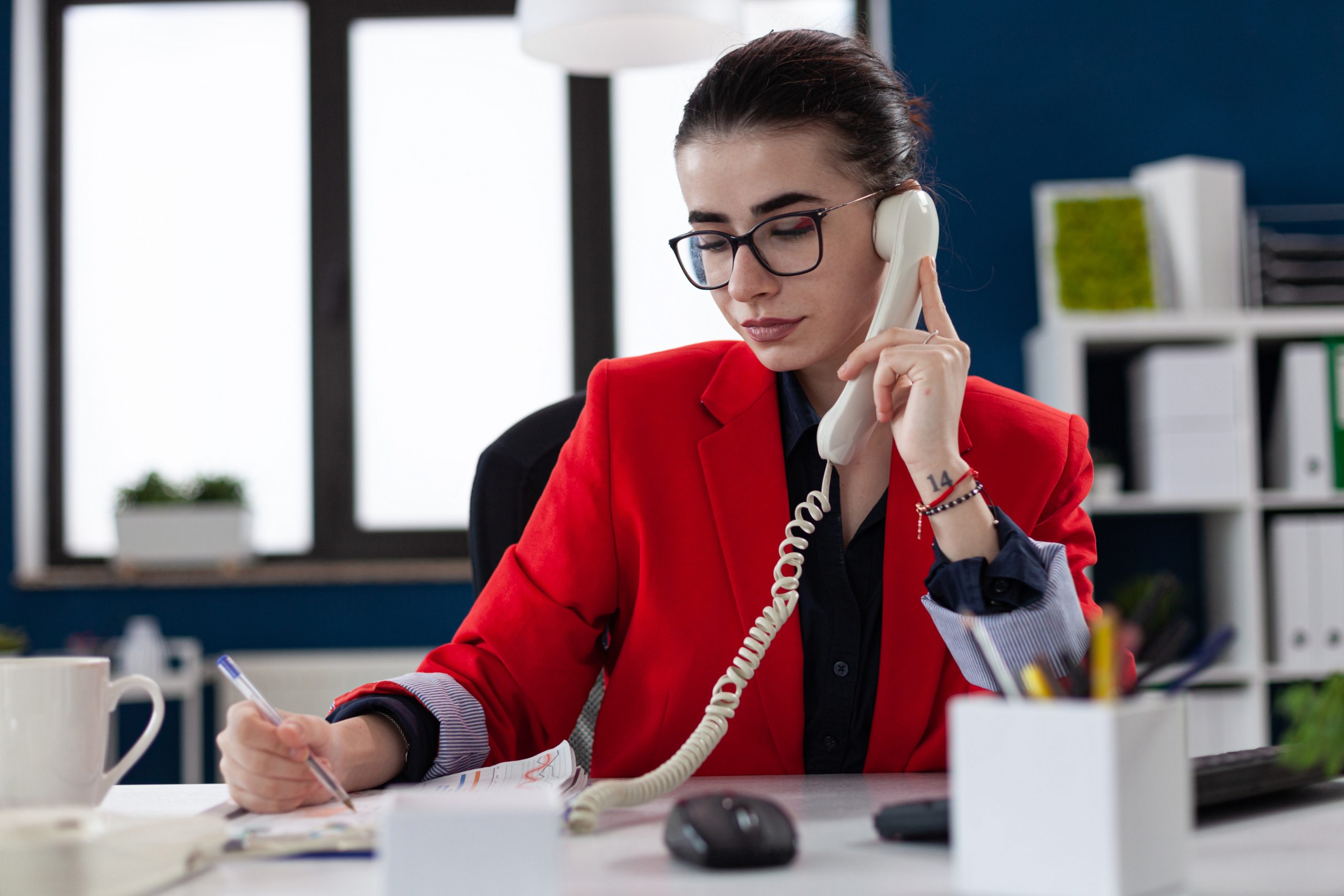 Businesswoman taking notes on clipboard sitting at desk in corporate office